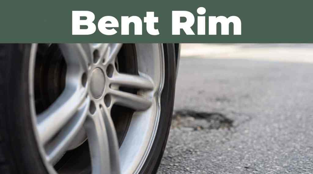 Close-up of a silver alloy wheel with a bent rim on rough asphalt road.
